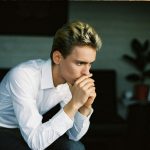 nervous young man leaning on hand and thinking in room