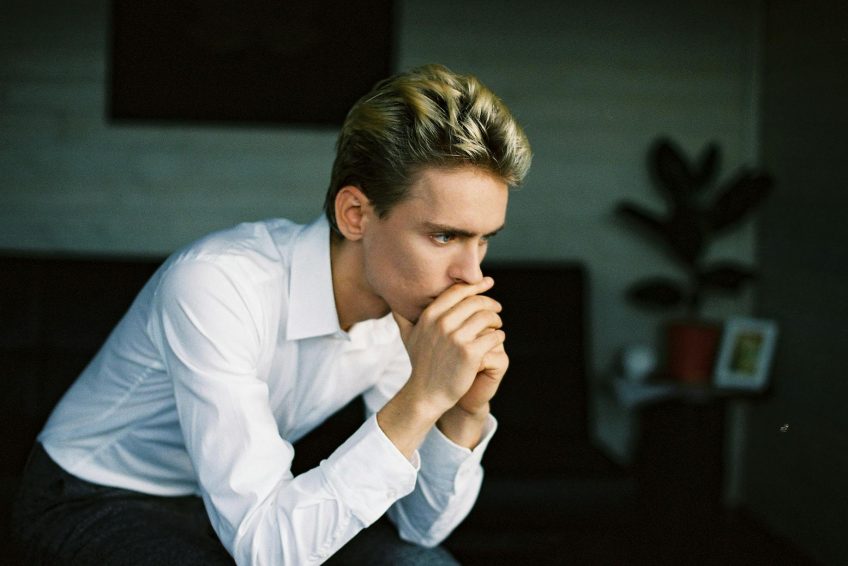 nervous young man leaning on hand and thinking in room