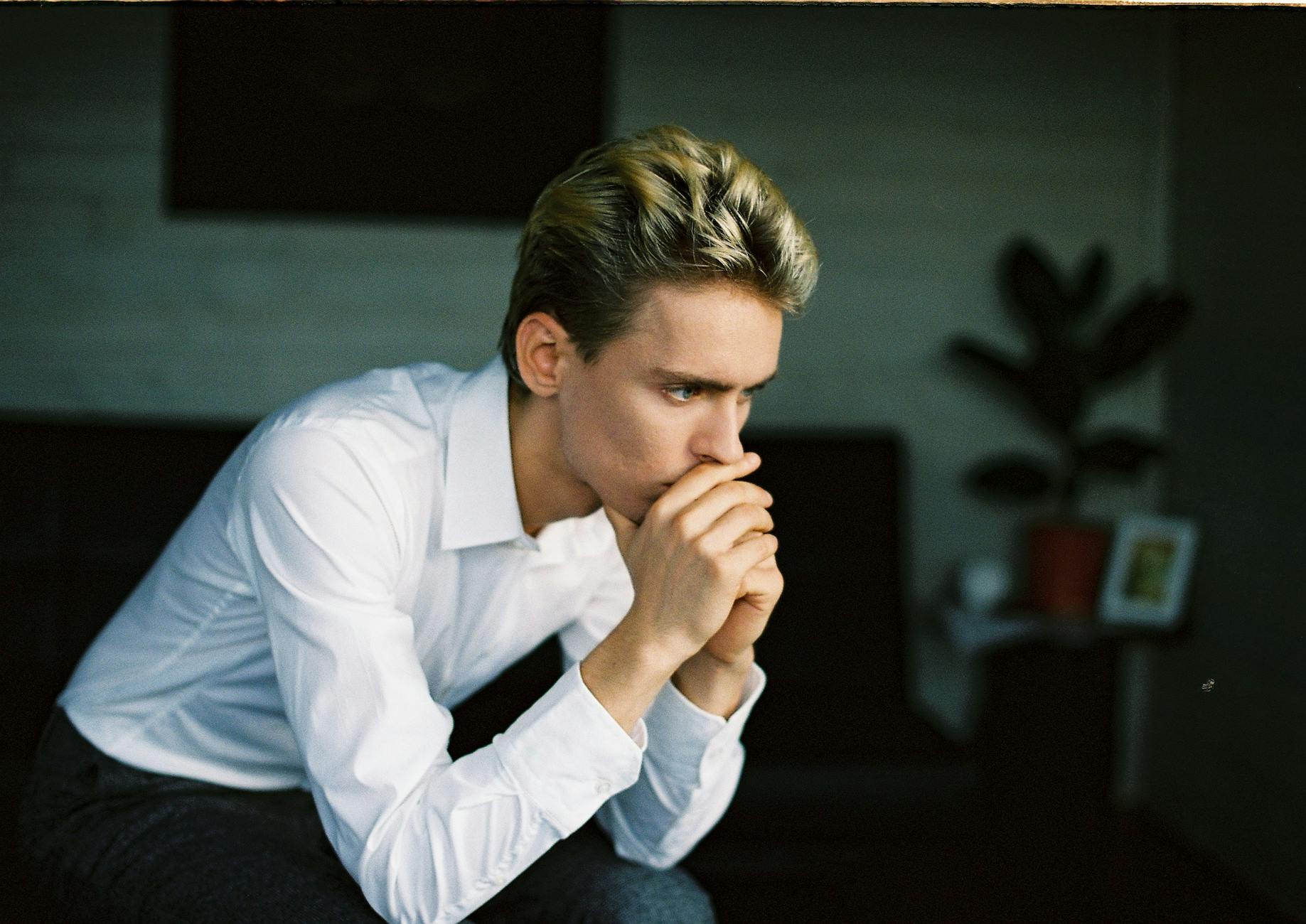 nervous young man leaning on hand and thinking in room